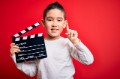 Young little boy kid filming video holding cinema director clapboard over isolated red background surprised with an idea or question pointing finger with happy face, number one